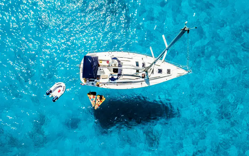 A sailing yacht at anchor in clear turquoise water, seen from above